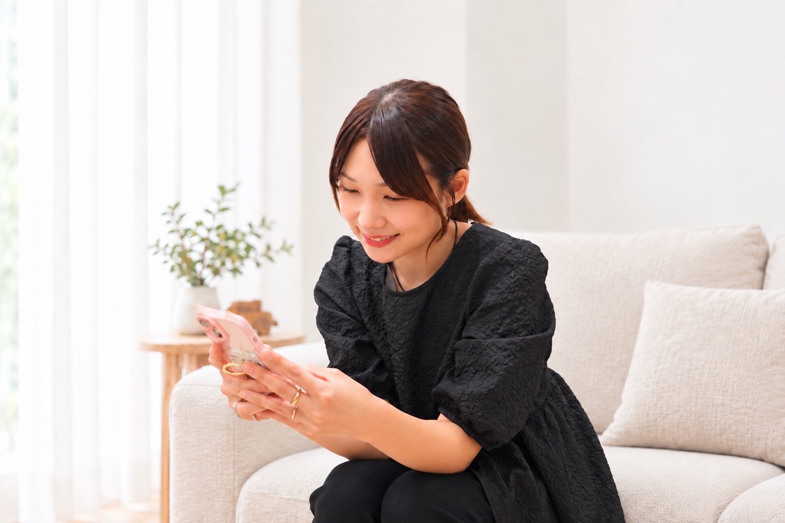 自宅のソファでスマートフォンを見ながら微笑む女性