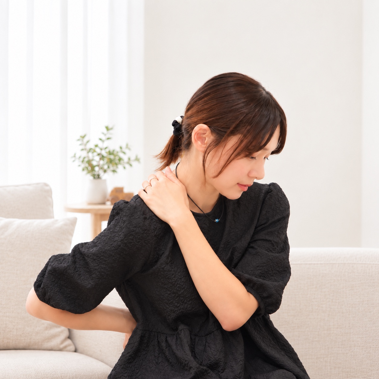 肩と腰に手を添えて体の不調を気にする女性